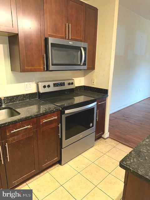 kitchen with appliances with stainless steel finishes, dark stone counters, sink, and light hardwood / wood-style flooring