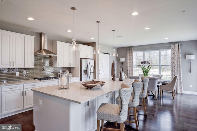 kitchen featuring hanging light fixtures, dark wood-type flooring, stainless steel appliances, white cabinets, and wall chimney exhaust hood