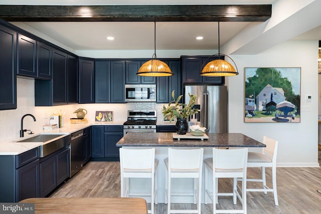 kitchen with appliances with stainless steel finishes, sink, pendant lighting, light hardwood / wood-style flooring, and a center island