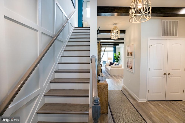 stairs featuring an inviting chandelier, beam ceiling, and wood-type flooring