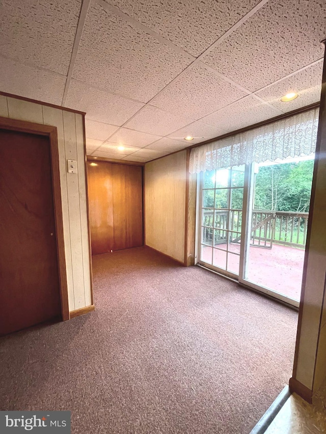 carpeted empty room featuring a paneled ceiling and wooden walls