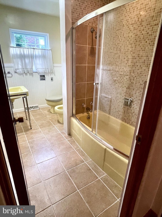 bathroom featuring tile patterned flooring, toilet, shower / bath combination with glass door, and a bidet