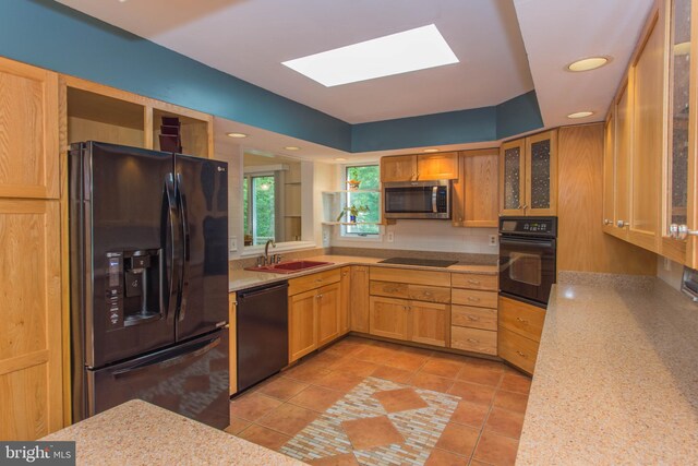 kitchen featuring light stone counters, light tile flooring, a skylight, black appliances, and sink