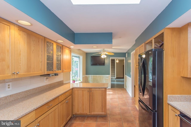 kitchen featuring light stone counters, black fridge, ceiling fan, tasteful backsplash, and light tile floors