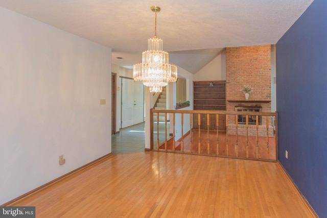 spare room featuring a chandelier, hardwood / wood-style flooring, brick wall, and vaulted ceiling