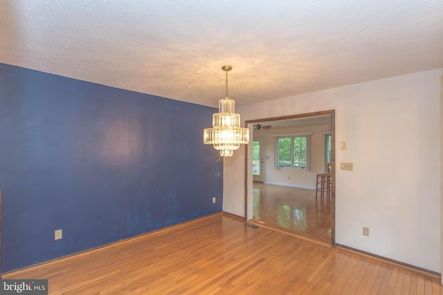 unfurnished room featuring an inviting chandelier, hardwood / wood-style floors, and a textured ceiling