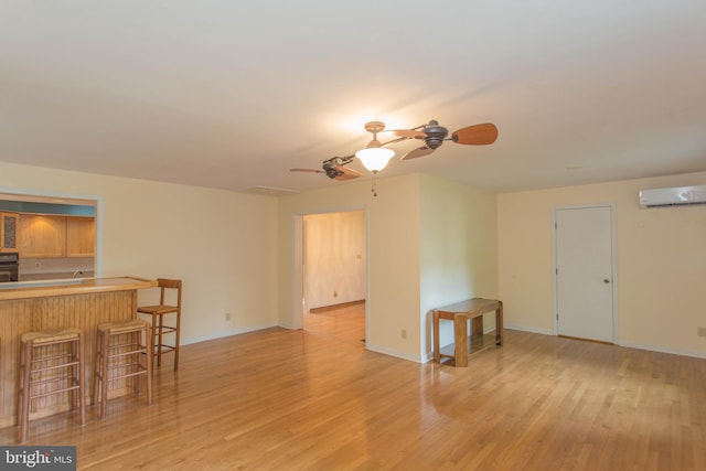 unfurnished room featuring a wall mounted air conditioner, ceiling fan, and light hardwood / wood-style flooring