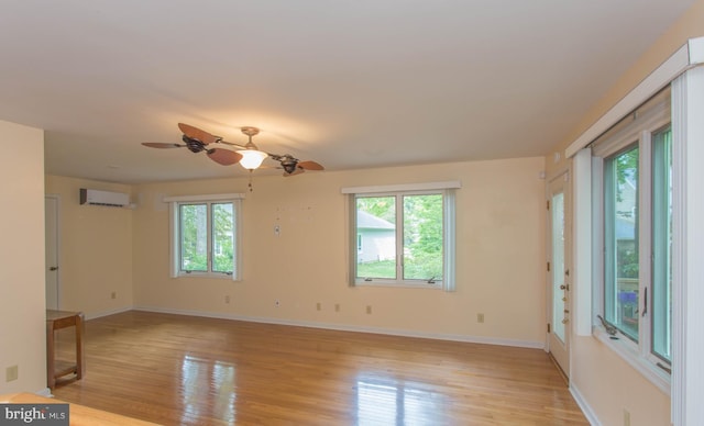 empty room featuring a healthy amount of sunlight, ceiling fan, light wood-type flooring, and a wall mounted air conditioner