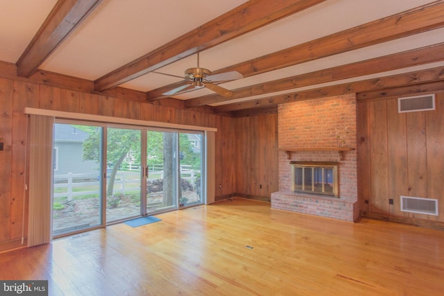 unfurnished living room with light wood-type flooring, beamed ceiling, wooden walls, a brick fireplace, and ceiling fan