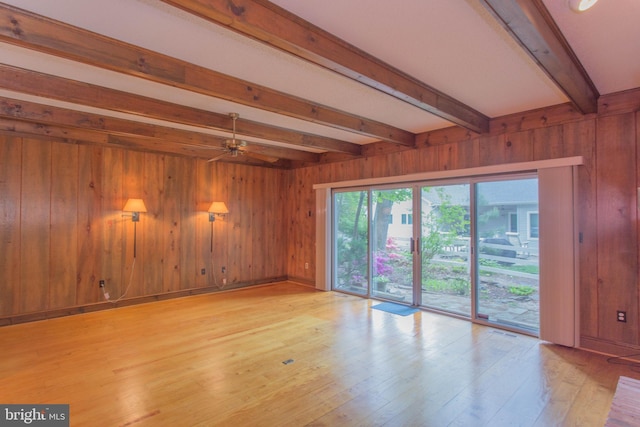 empty room featuring beamed ceiling, light wood-type flooring, and wood walls