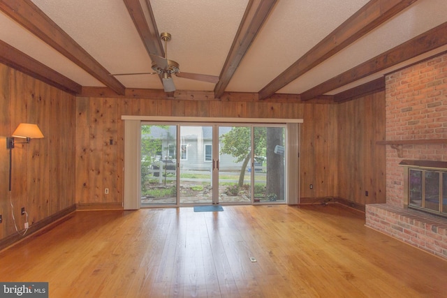 unfurnished living room with a fireplace, beamed ceiling, wood walls, and light wood-type flooring