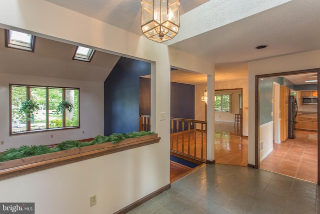 hallway featuring a skylight, tile flooring, a wealth of natural light, and a chandelier