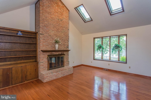 unfurnished living room with brick wall, light wood-type flooring, and lofted ceiling with skylight