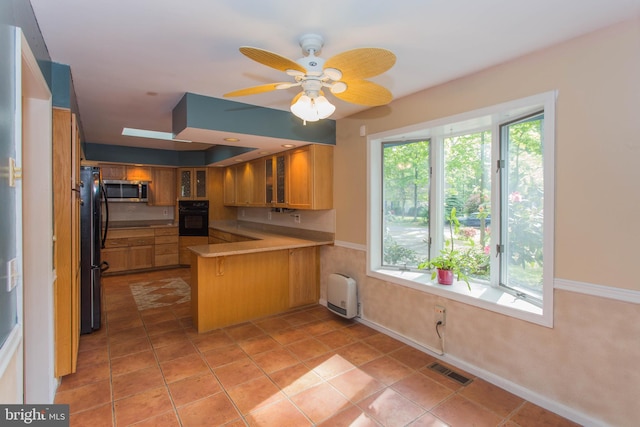 kitchen featuring kitchen peninsula, ceiling fan, tile flooring, black appliances, and radiator heating unit