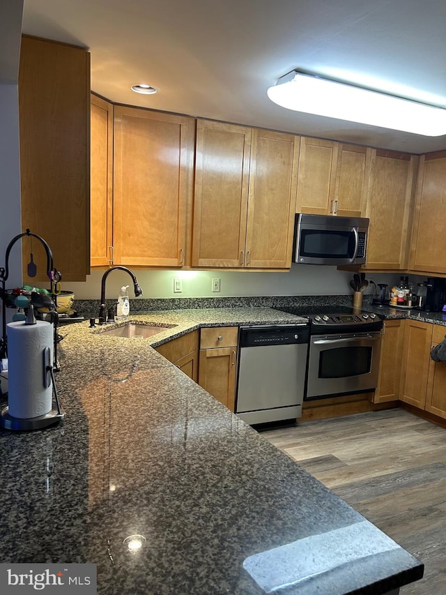 kitchen featuring dark stone countertops, light hardwood / wood-style floors, stainless steel appliances, and sink