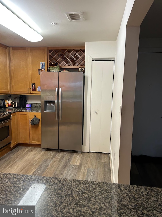 kitchen featuring light hardwood / wood-style floors, dark stone counters, and stainless steel appliances