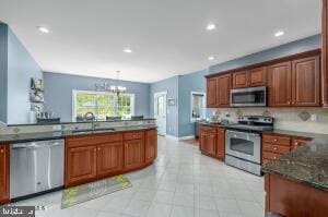 kitchen with stainless steel appliances, light tile flooring, pendant lighting, a notable chandelier, and sink