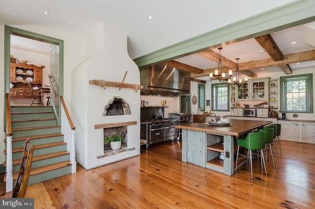 kitchen featuring a healthy amount of sunlight, beamed ceiling, wall chimney exhaust hood, and light hardwood / wood-style flooring