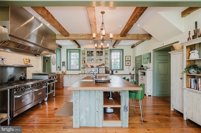 kitchen with wall chimney range hood, a kitchen bar, an island with sink, high end stainless steel range, and pendant lighting