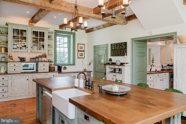 kitchen with hanging light fixtures, stainless steel microwave, butcher block countertops, hardwood / wood-style flooring, and sink