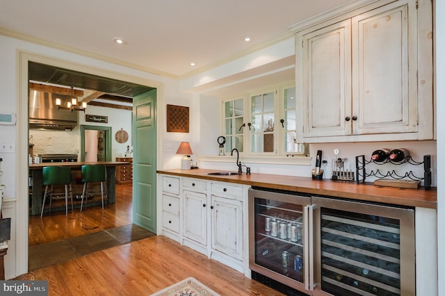 bar with hanging light fixtures, wine cooler, sink, and wood counters