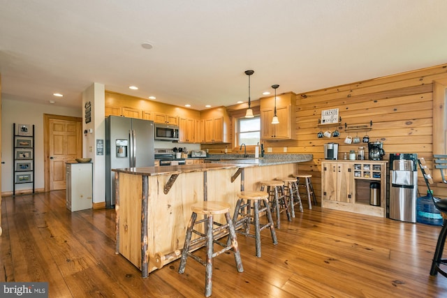 kitchen featuring stainless steel appliances, decorative light fixtures, a kitchen breakfast bar, light hardwood / wood-style flooring, and kitchen peninsula