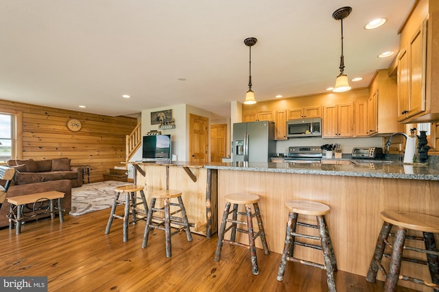 kitchen featuring light wood-type flooring, a breakfast bar, stainless steel appliances, and dark stone countertops