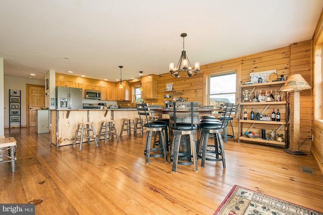 dining area featuring light wood finished floors, a chandelier, a wealth of natural light, and wood walls