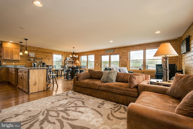 living room featuring wooden walls, dark wood-style flooring, a wood stove, a chandelier, and recessed lighting