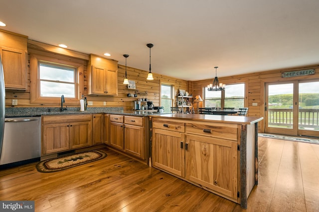 kitchen with dishwasher, sink, wood walls, light hardwood / wood-style flooring, and decorative light fixtures