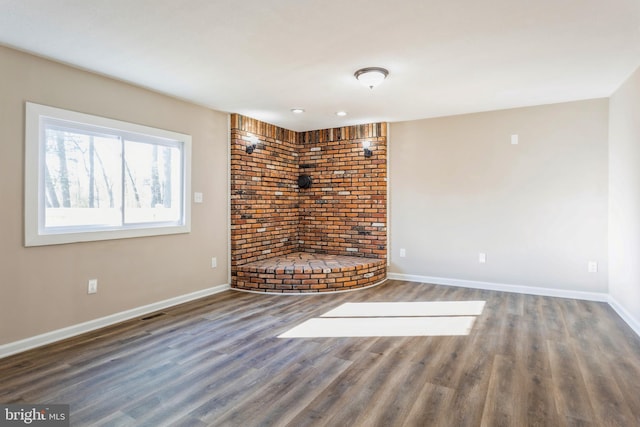 spare room featuring dark wood-type flooring and brick wall