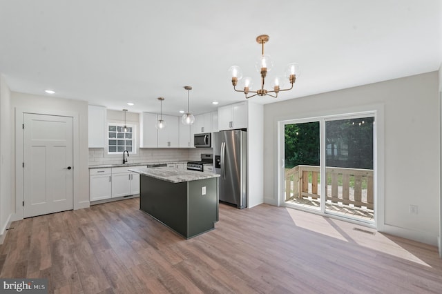 kitchen with white cabinets, decorative light fixtures, a center island, and appliances with stainless steel finishes