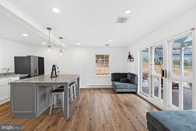 kitchen featuring stainless steel fridge, light stone counters, white cabinets, light hardwood / wood-style floors, and hanging light fixtures