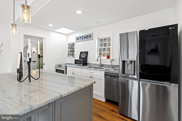 kitchen featuring appliances with stainless steel finishes, dark hardwood / wood-style flooring, light stone counters, white cabinets, and hanging light fixtures