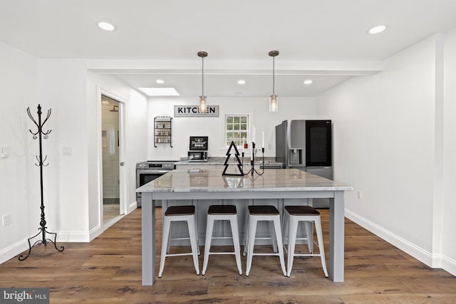 kitchen with a kitchen breakfast bar, light stone counters, hanging light fixtures, and dark hardwood / wood-style floors