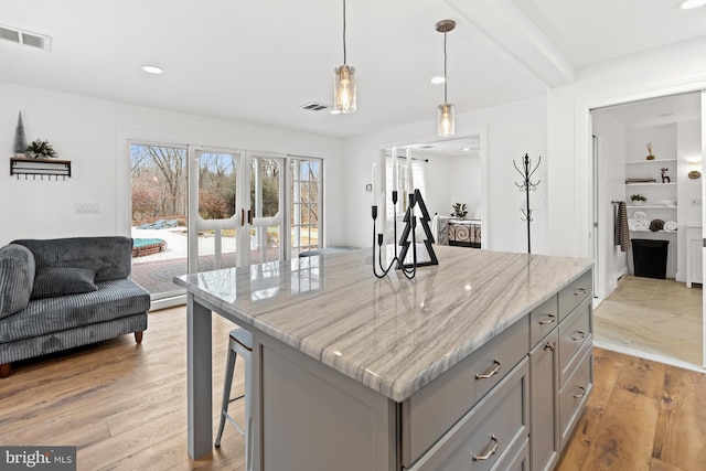 kitchen with light stone countertops, light hardwood / wood-style floors, hanging light fixtures, and beamed ceiling