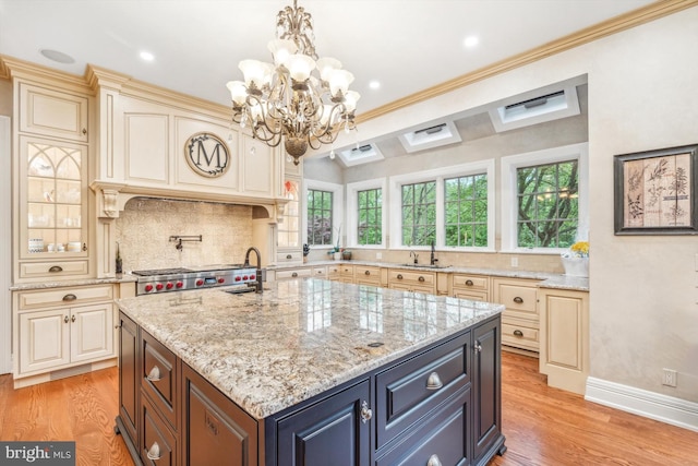 kitchen featuring crown molding, hanging light fixtures, light hardwood / wood-style flooring, an island with sink, and light stone counters