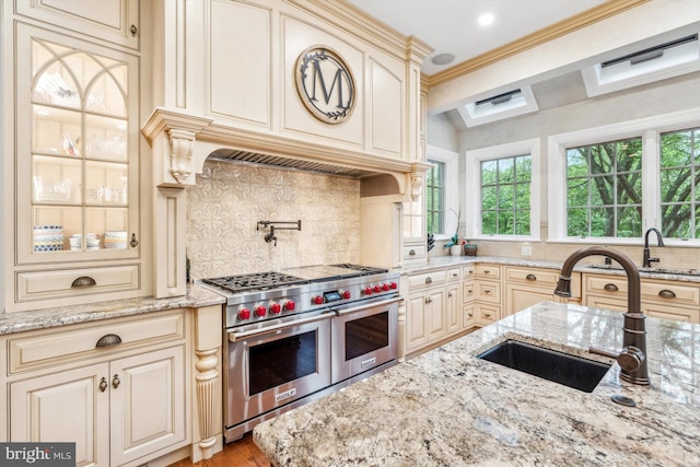 kitchen with decorative backsplash, double oven range, light stone countertops, and cream cabinets