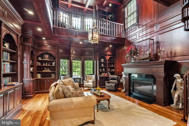 living area with coffered ceiling, wooden walls, light hardwood / wood-style flooring, built in features, and beam ceiling