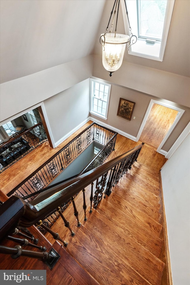 staircase featuring hardwood / wood-style flooring, an inviting chandelier, plenty of natural light, and lofted ceiling