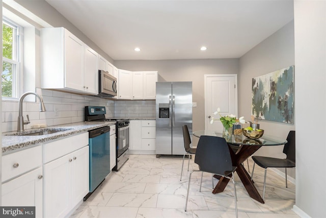 kitchen with decorative backsplash, light stone countertops, stainless steel appliances, sink, and white cabinets