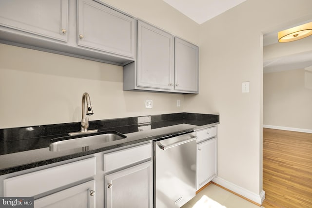 kitchen featuring sink, stainless steel dishwasher, light hardwood / wood-style flooring, gray cabinets, and dark stone countertops