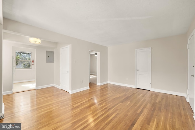 empty room featuring electric panel, ceiling fan, light hardwood / wood-style floors, and a textured ceiling