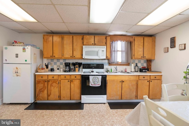 kitchen featuring white appliances, sink, backsplash, and a drop ceiling