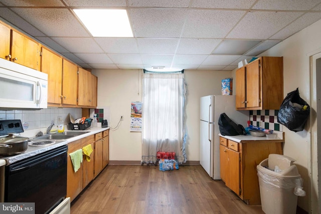 kitchen with a paneled ceiling, light hardwood / wood-style flooring, white appliances, backsplash, and sink