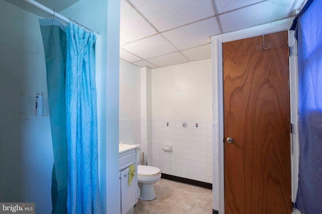 bathroom featuring tile flooring, a paneled ceiling, tile walls, vanity, and toilet