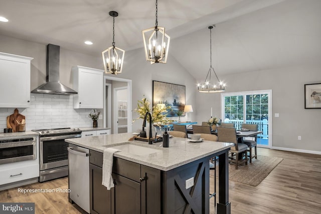 kitchen with light wood-type flooring, lofted ceiling, white cabinetry, wall chimney exhaust hood, and appliances with stainless steel finishes