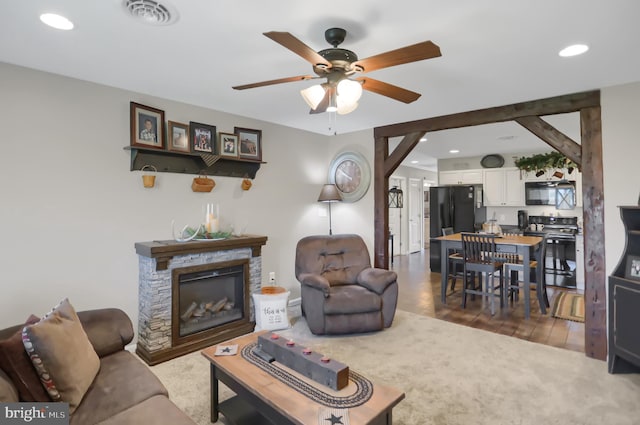 living room featuring a stone fireplace, hardwood / wood-style flooring, and ceiling fan