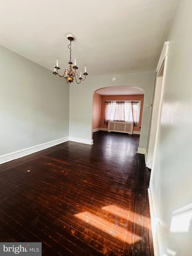 unfurnished room with dark hardwood / wood-style floors, radiator, and an inviting chandelier