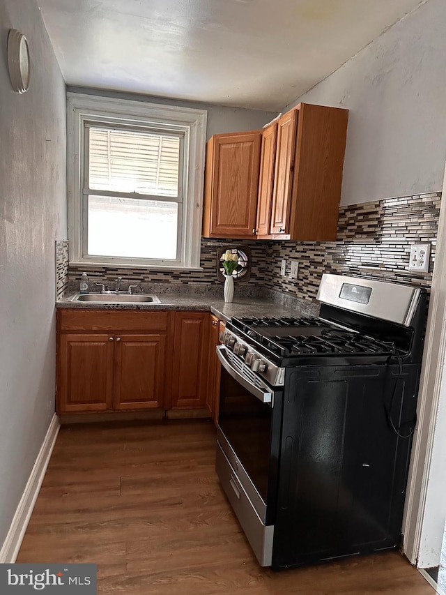 kitchen with backsplash, sink, gas range, and wood-type flooring